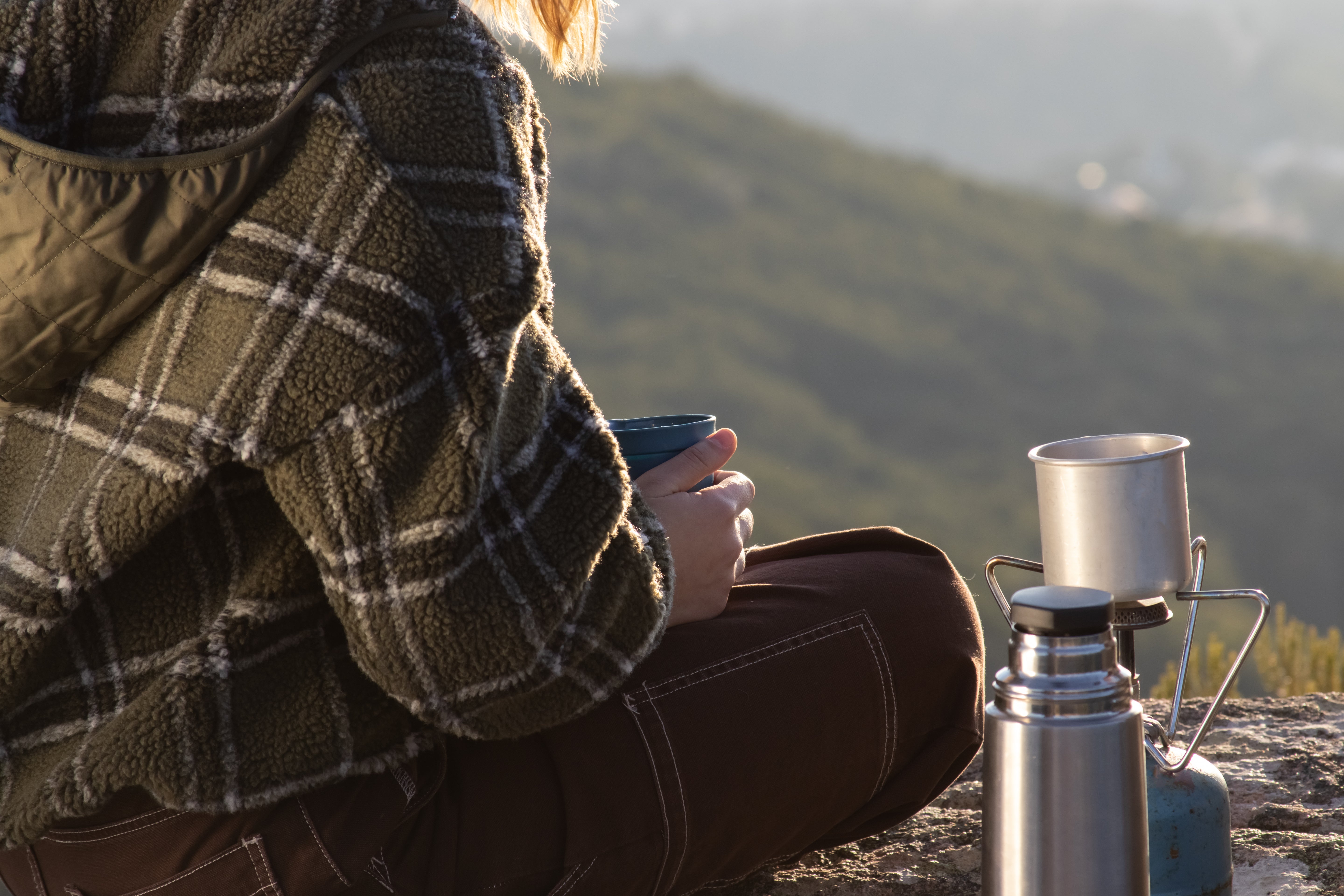 Woman wearing sweatshirt drinking coffee on mountain top.